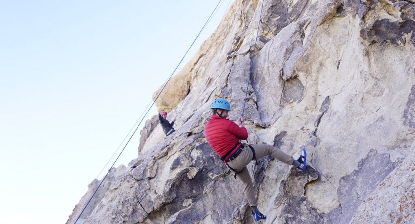 A person wearing safety gear is secured by ropes as they rock climb